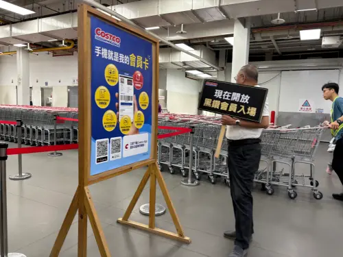 好市多賣場工作人員手持「現在開放黑鑽會員入場」告示牌,身旁擺放手機電子會員卡宣傳看板 ▲台灣好市多提供黑鑽卡會員上午 9 點提早 1 小時入場服務,成為許多民眾搶購熱門熟食與爆紅商品的早鳥秘訣。(圖/記者徐銘穗攝)